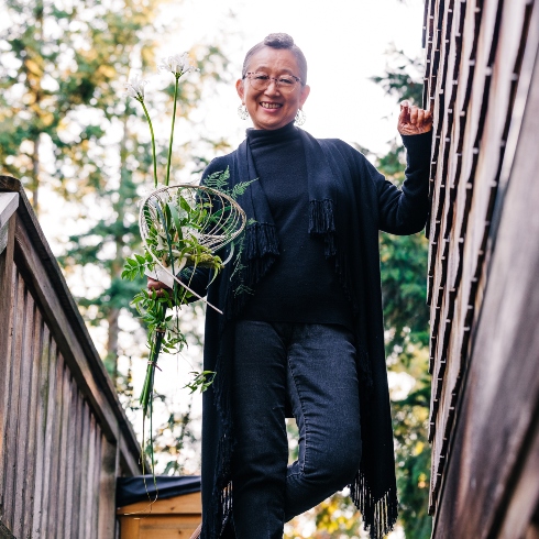 Hitomi Gilliam and DESIGN358 Floral artist and educator Hitomi Gilliam holding a plant while standing on an outdoor staircase